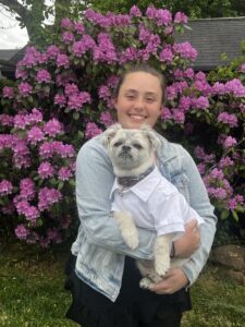 Person holding a small dog in front of flowers
